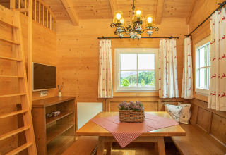 Accogliente baita in legno con tavolo da pranzo, finestre panoramiche, TV e tende alpine a Camp MondSeeLand.