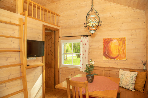 Gemütliche Holzhütte mit Essbereich, Leiter zum Schlafboden und Fensterblick im Camp MondSeeLand.
