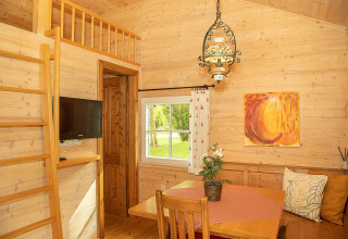 Gemütliche Holzhütte mit Essbereich, Leiter zum Schlafboden und Fensterblick im Camp MondSeeLand.