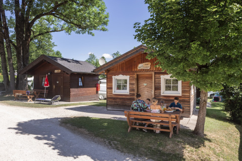 Familie isst vor Holzhütte auf dem Camp MondSeeLand, Glamping- und Campingplatz in Österreich.