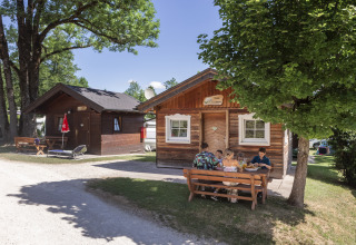 Famiglia mangia davanti a una baita in legno al Camp MondSeeLand, glamping e campeggio in Austria.