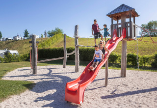 Familias disfrutan en un parque infantil soleado con tobogán en Camp MondSeeLand glamping en Austria.