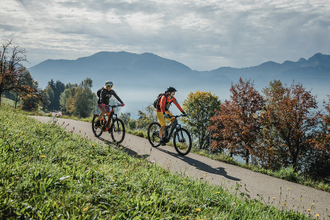 Due ciclisti vicino a Camp MondSeeLand - Kampeerhutten Oostenrijk, immersi nella natura con montagne sullo sfondo.