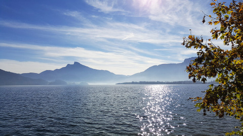 View of lake and mountains at Camp MondSeeLand - Kampeerhutten Oostenrijk, with sunlight glistening on water.