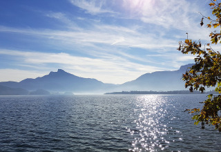 Vue sur le lac et les montagnes au Camp MondSeeLand - Kampeerhutten Oostenrijk, avec reflets de soleil sur l’eau.