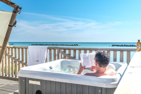 Un homme se détend dans un jacuzzi face à la mer au Villa Alwin Beach Resort en tentes de luxe à Le Marche.