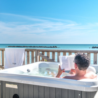 Un homme se détend dans un jacuzzi face à la mer au Villa Alwin Beach Resort en tentes de luxe à Le Marche.