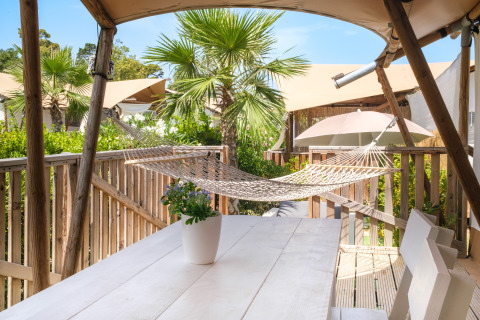 Terras met hangmat, houten tafel en palmbomen bij Villa Alwin Beach Resort, luxe lodgetent in Le Marche.