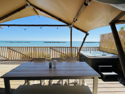 Buiten op luxe lodgetent-terras met eettafel en jacuzzi aan het strand bij Villa Alwin Beach Resort.