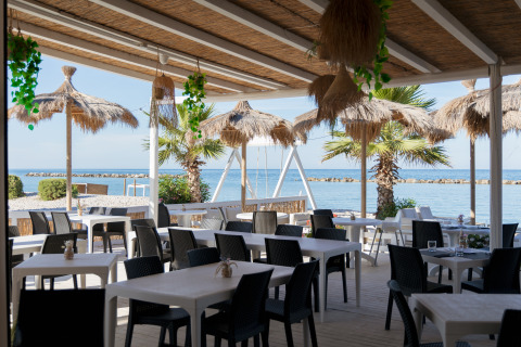 Espace repas extérieur avec parasols en paille et vue sur la mer à Villa Alwin Beach Resort à Le Marche.