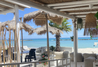 Buitenlounge met rieten parasols en zeezicht bij Villa Alwin Beach Resort - lodgetenten in Le Marche, Italië.