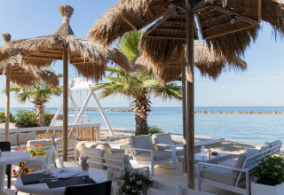 Outdoor-Loungebereich mit Strohdächern und Meeresblick im Villa Alwin Beach Resort in Le Marche, Italien.