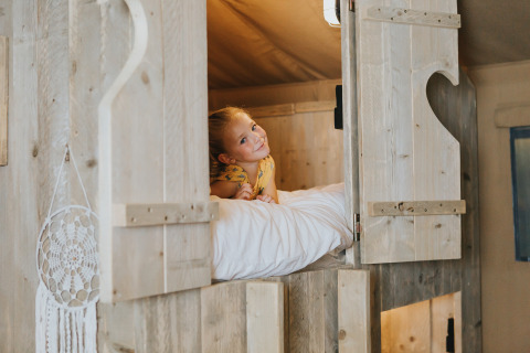 Et barn ligger i en hyggelig seng i en træhytte på Villa Alwin Beach Resort, Luxe lodgetelte i Le Marche.