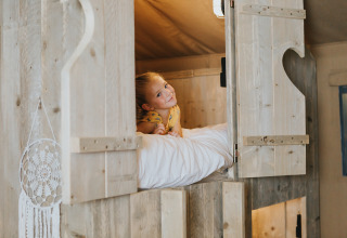 Un enfant est allongé dans un lit en bois douillet au Villa Alwin Beach Resort en tente lodge à Le Marche, Italie.