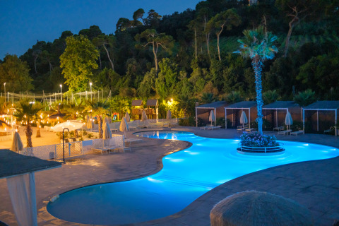 Piscina iluminada y tiendas glamping de lujo en Villa Alwin Beach Resort, Le Marche, Italia, por la noche.
