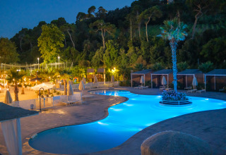 Piscine éclairée et tentes de glamping de luxe à la Villa Alwin Beach Resort dans les Marches, Italie, de nuit.