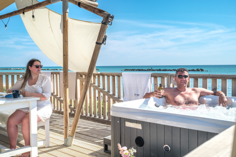 Coppia che si gode il glamping di lusso presso Villa Alwin Beach Resort a Le Marche con vasca idromassaggio e vista mare.