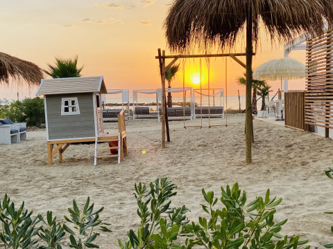 Atardecer en la playa del Villa Alwin Beach Resort con casita de juegos, columpios y palmeras en Le Marche.