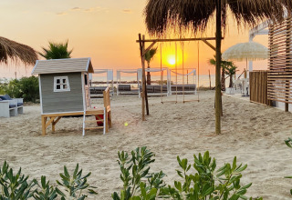 Tramonto sulla spiaggia di Villa Alwin Beach Resort con casetta, altalene e palme nelle Marche, Italia.