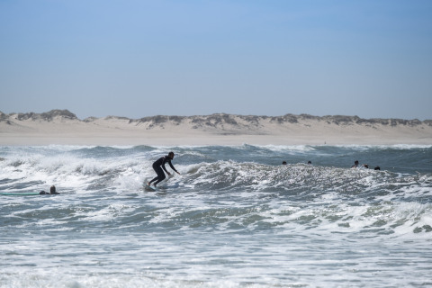 Surfer pakt golven bij het strand vlakbij Huttopia Lagoa de Óbidos Glamping Portugal bij helder weer.