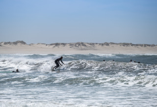 Surfista disfrutando las olas en la playa cerca de Huttopia Lagoa de Óbidos Glamping Portugal bajo cielo claro.