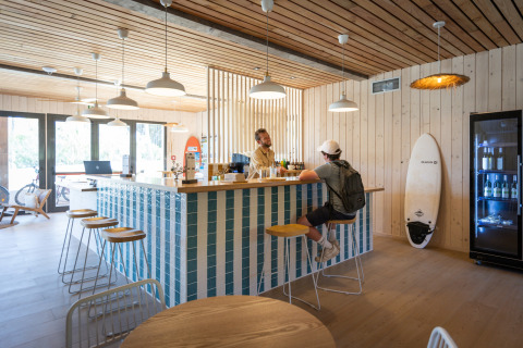 Coin bar moderne à Huttopia Lagoa de Óbidos Glamping Portugal, déco bois clair et planche de surf.