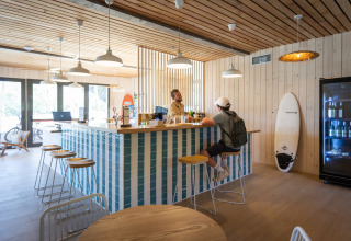 Modern bar area at Huttopia Lagoa de Óbidos Glamping Portugal, light wood decor and a surfboard.