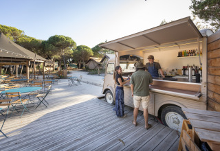 Udendørs madvogn og spisested ved Huttopia Lagoa de Óbidos - Glamping Portugal med gæster og træer.