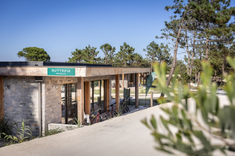 Receptiegebouw van Huttopia Lagoa de Óbidos Glamping Portugal tussen de dennen en onder een blauwe lucht.