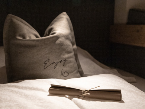 Gezellig kussen en opgerold papier op bed bij Wander- & Wellnesshotel Gassner - Boomhut Oostenrijk glamping.