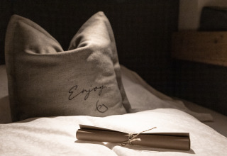Cozy pillow and rolled paper on bed in Wander- & Wellnesshotel Gassner - Boomhut Oostenrijk glamping room.