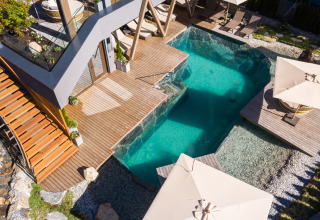 Hébergement glamping de luxe au Wander- & Wellnesshotel Gassner avec piscine moderne, terrasse en bois et transats.