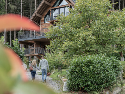 Un couple marche main dans la main vers le Wander- & Wellnesshotel Gassner - Boomhut Oostenrijk, entouré de verdure.