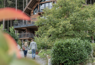 Una coppia cammina mano nella mano verso Wander- & Wellnesshotel Gassner - Boomhut Oostenrijk, immersa nel verde.
