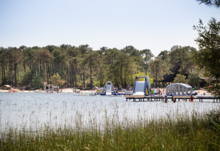 Vue sur le lac avec jeux gonflables aquatiques à Huttopia Lac de Carcans glamping, entouré de pins.
