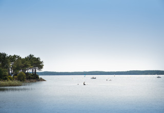 Uitzicht op het meer bij Huttopia Lac de Carcans Glamping Aquitaine met boten en zwemmers onder blauwe hemel.