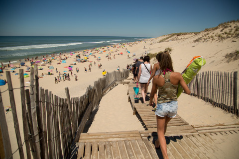 Persone su una passerella verso la spiaggia di Huttopia Lac de Carcans - Glamping Aquitaine in una giornata estiva.