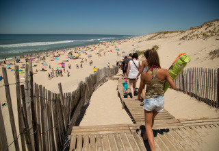 Des gens descendent vers la plage sur une passerelle à Huttopia Lac de Carcans - Glamping Aquitaine en été.