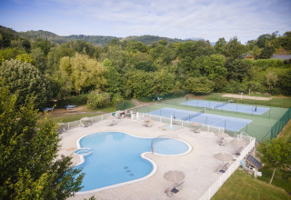 Huttopia Royat - Glamping Auvergne zeigt Pool und Tennisplätze, eingebettet in die grüne Naturlandschaft.