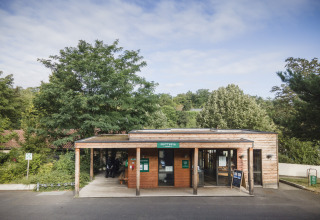 Entrada de Huttopia Royat - Glamping Auvergne con edificio de madera moderna rodeado de árboles verdes.