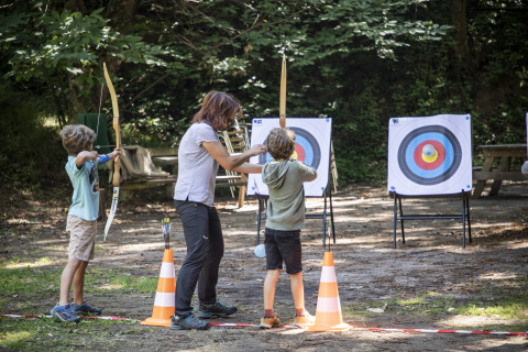 Bambini imparano il tiro con l’arco all’aperto con un istruttore presso Huttopia Royat - Glamping Auvergne.