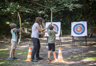 Kinderen leren boogschieten buiten met een begeleider bij Huttopia Royat - Glamping Auvergne camping.
