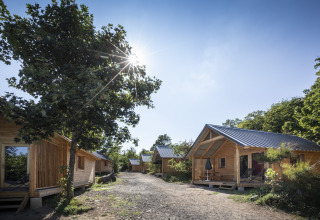 Sonnige Glamping-Unterkünfte aus Holz bei Huttopia Royat - Glamping Auvergne in einer grünen Naturkulisse.