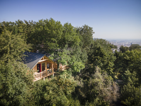 Glamping accommodatie in houten hut, omgeven door bomen met uitzicht op de stad, Huttopia Royat - Glamping Auvergne.