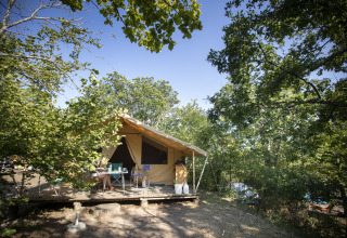 Glampingaccommodatie Huttopia Royat - Glamping Auvergne in het bos, met houten veranda en buitenmeubilair.