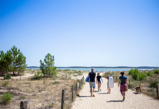 Familia caminando hacia la playa en Huttopia Oléron les Chênes Verts - Glamping Nouvelle Aquitaine bajo el sol.