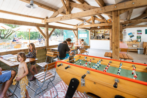 Familles profitent de jeux de société et baby-foot sous l’espace commun de Huttopia Oléron les Chênes Verts.