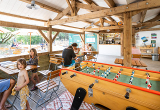 Gezinnen genieten van spelletjes en ontspanning in de lounge van Huttopia Oléron les Chênes Verts Glamping.