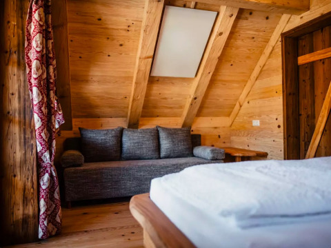 Interior de madera con sofá y cama en el glamping s'Baumhaus Dörfle - Boomhutten Zwarte Woud.