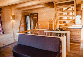 Vue intérieure d’une cabane glamping chaleureuse avec murs en bois, escalier et canapé au s'Baumhaus Dörfle.